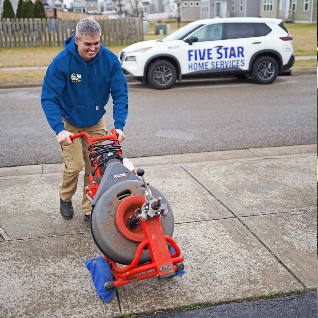 Plumber with a sewer inspection tool walking on a driveway